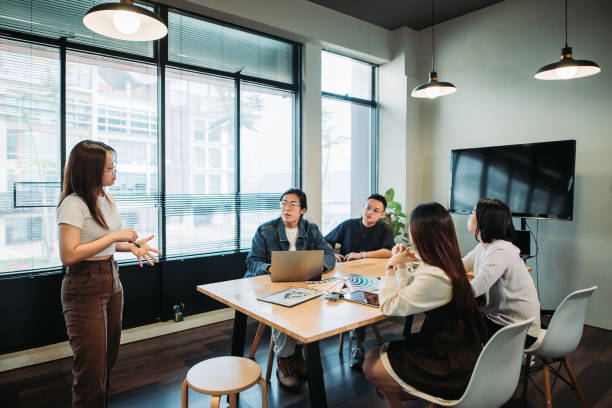 wide shot of young woman standing and having discussion with team